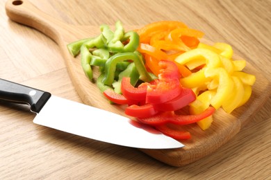 Photo of Slices of fresh colorful bell peppers and knife on wooden table, closeup