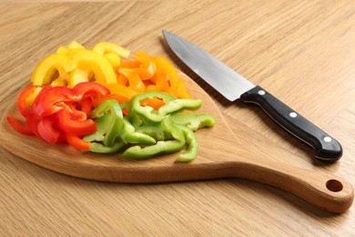 Photo of Slices of fresh colorful bell peppers and knife on wooden table, closeup