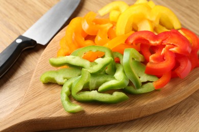 Photo of Slices of fresh colorful bell peppers and knife on wooden table, closeup