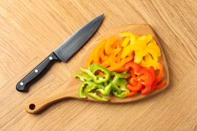 Photo of Slices of fresh colorful bell peppers and knife on wooden table, flat lay