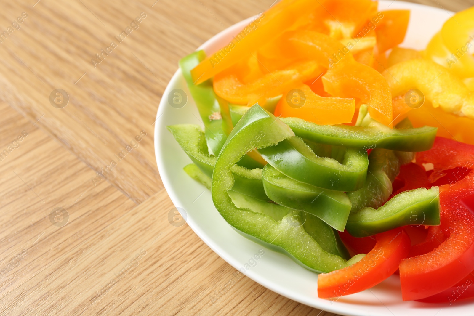 Photo of Slices of fresh colorful bell peppers on wooden table, closeup. Space for text