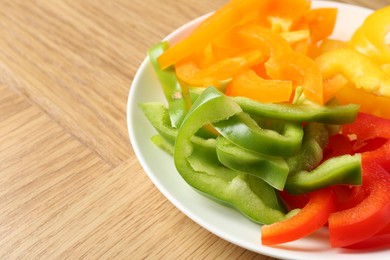 Photo of Slices of fresh colorful bell peppers on wooden table, closeup. Space for text