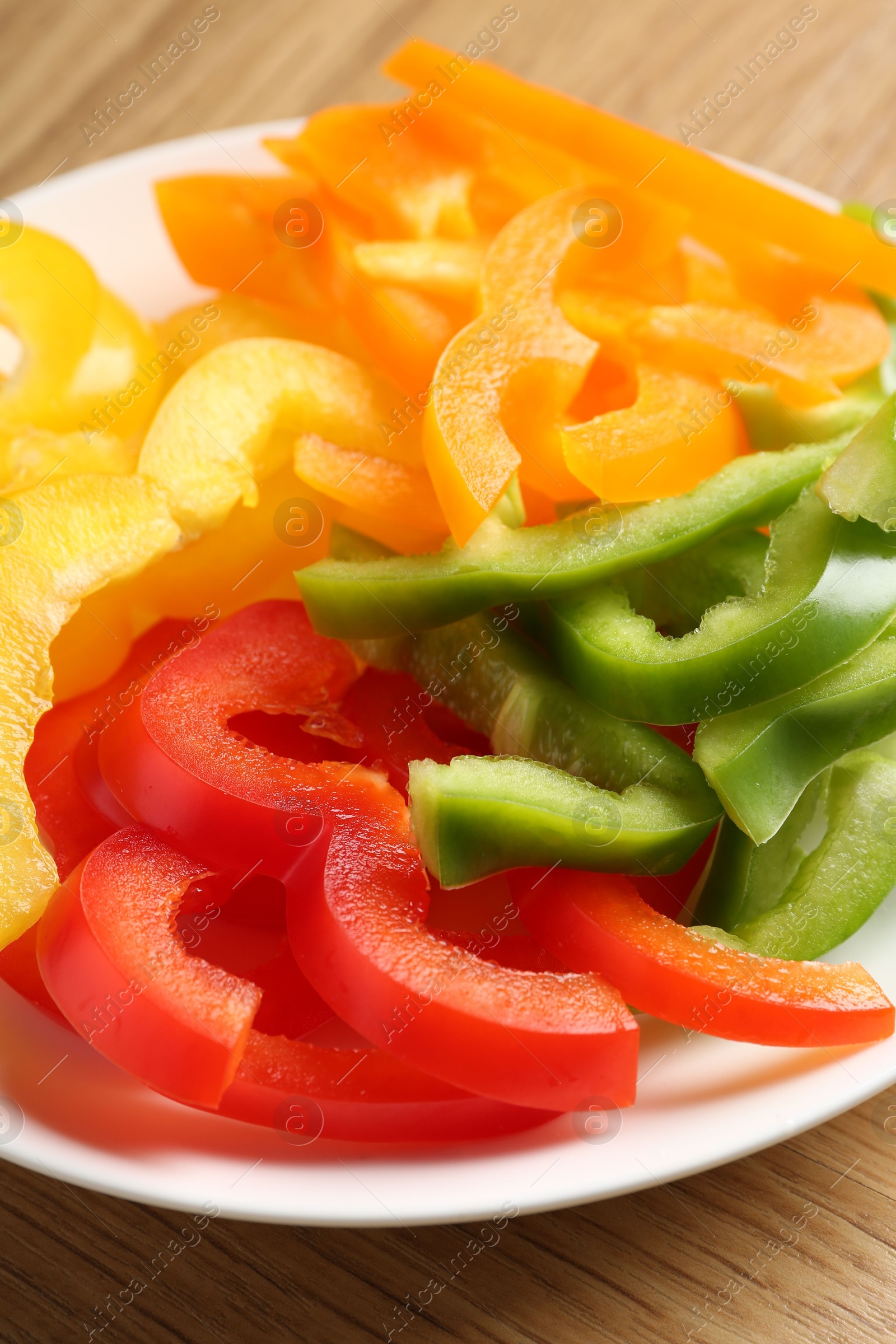 Photo of Slices of fresh colorful bell peppers on wooden table, closeup