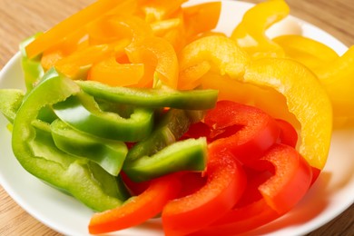 Photo of Slices of fresh colorful bell peppers on wooden table, closeup