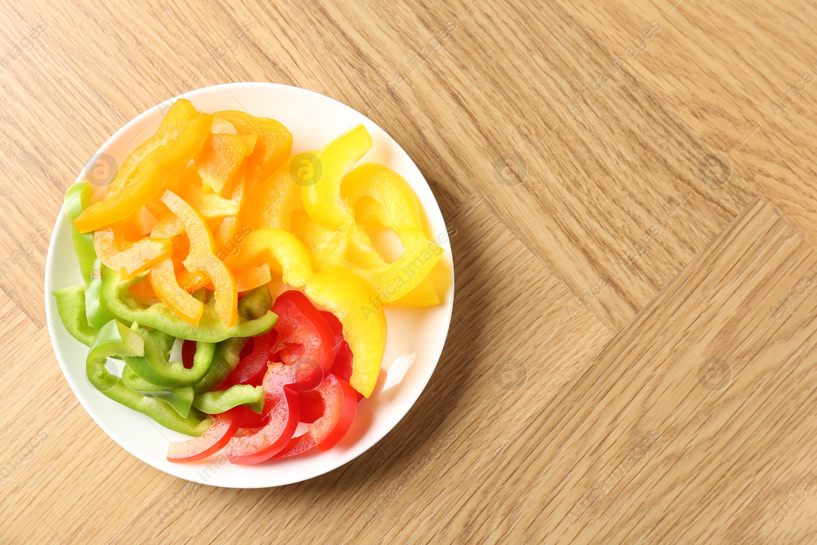 Photo of Slices of fresh colorful bell peppers on wooden table, top view. Space for text