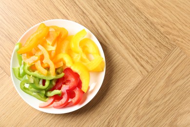 Photo of Slices of fresh colorful bell peppers on wooden table, top view. Space for text