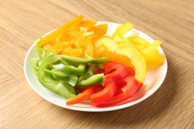 Photo of Slices of fresh colorful bell peppers on wooden table, closeup