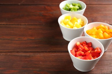 Photo of Pieces of fresh colorful bell peppers in bowls on wooden table, closeup. Space for text