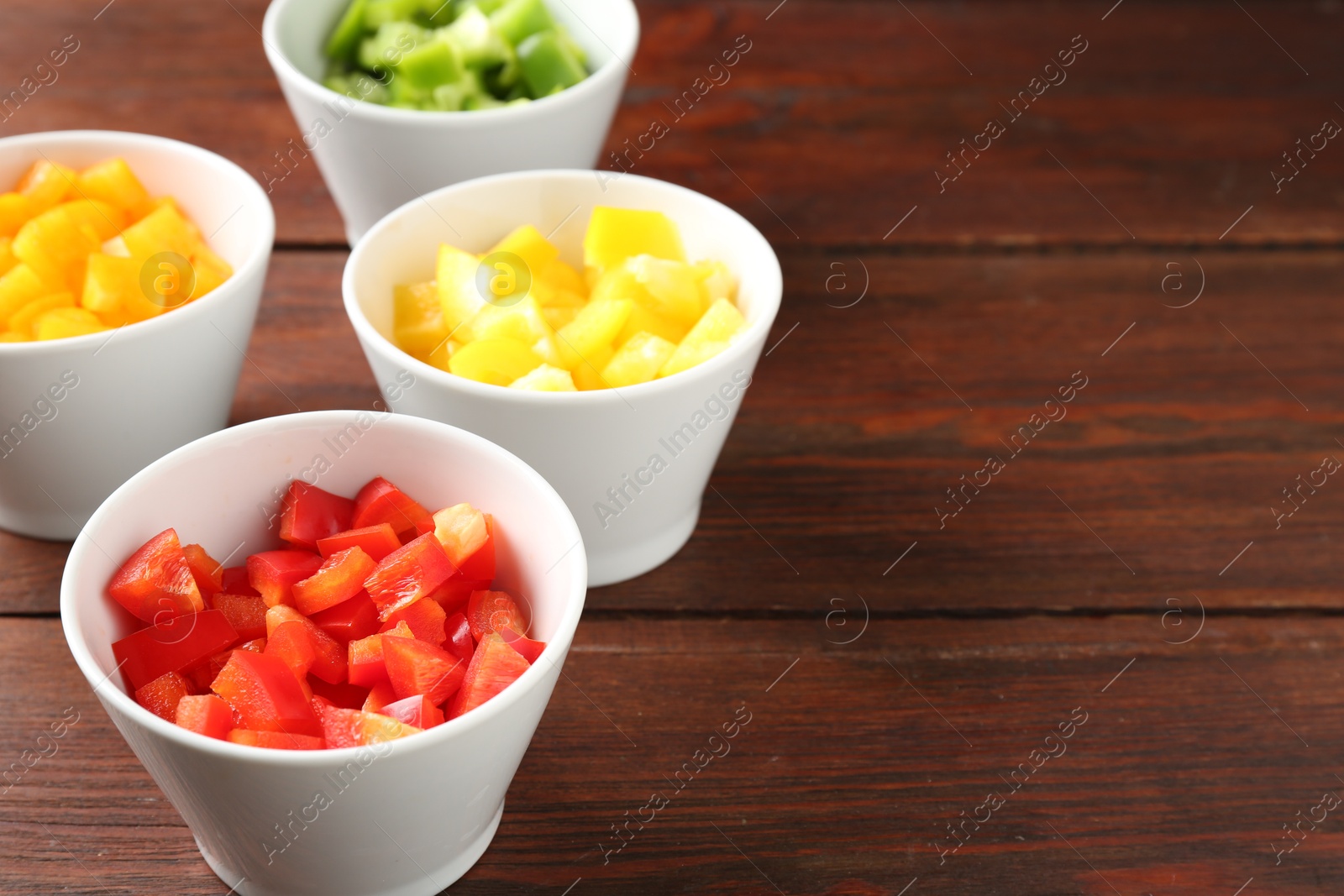 Photo of Pieces of fresh colorful bell peppers in bowls on wooden table, closeup. Space for text
