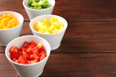 Photo of Pieces of fresh colorful bell peppers in bowls on wooden table, closeup. Space for text