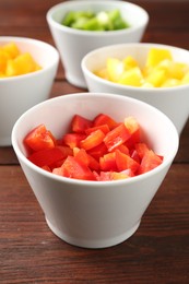 Photo of Pieces of fresh colorful bell peppers in bowls on wooden table, closeup