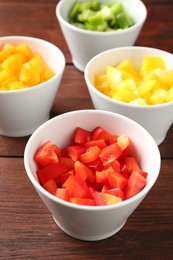 Photo of Pieces of fresh colorful bell peppers in bowls on wooden table, closeup