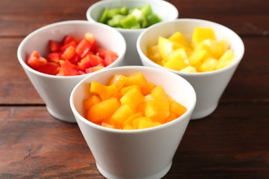 Photo of Pieces of fresh colorful bell peppers in bowls on wooden table, closeup