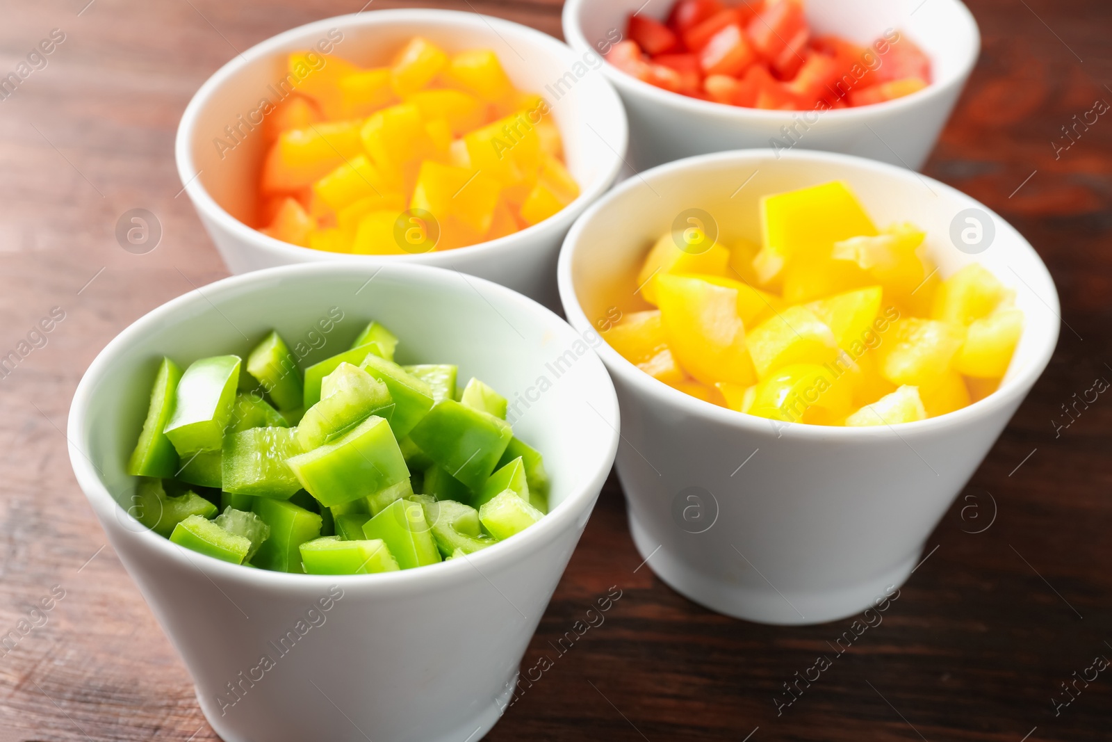 Pieces of fresh colorful bell peppers in bowls on wooden table, closeup Photo of Pieces of fresh colorful bell peppers in bowls on wooden table, closeup