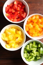 Photo of Pieces of fresh colorful bell peppers in bowls on wooden table, flat lay