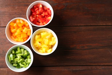 Photo of Pieces of fresh colorful bell peppers in bowls on wooden table, flat lay. Space for text