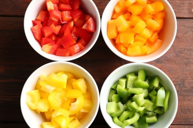 Photo of Pieces of fresh colorful bell peppers in bowls on wooden table, flat lay