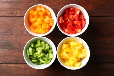 Photo of Pieces of fresh colorful bell peppers in bowls on wooden table, flat lay