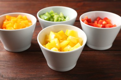 Photo of Pieces of fresh colorful bell peppers in bowls on wooden table, closeup