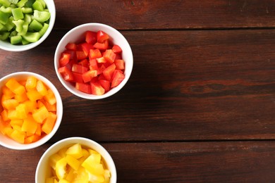 Photo of Pieces of fresh colorful bell peppers in bowls on wooden table, flat lay. Space for text
