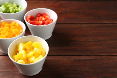 Photo of Pieces of fresh colorful bell peppers in bowls on wooden table, closeup. Space for text