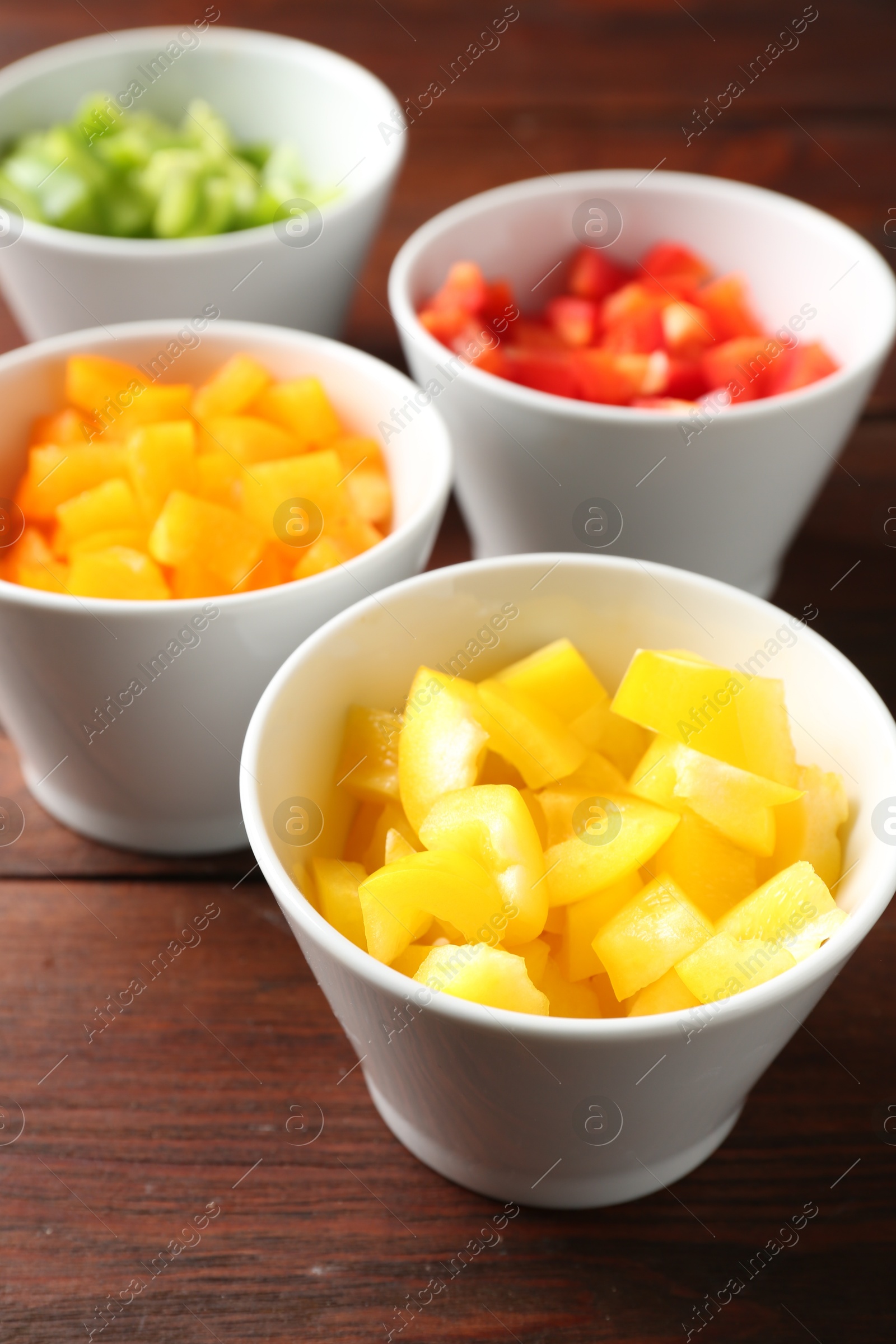 Pieces of fresh colorful bell peppers in bowls on wooden table, closeup Photo of Pieces of fresh colorful bell peppers in bowls on wooden table, closeup