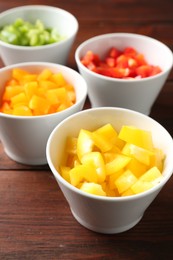Photo of Pieces of fresh colorful bell peppers in bowls on wooden table, closeup