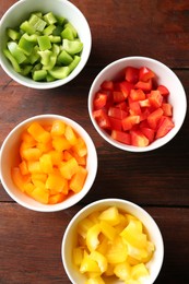 Photo of Pieces of fresh colorful bell peppers in bowls on wooden table, flat lay