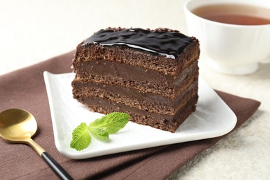 Photo of Piece of chocolate cake served with mint, spoon and tea on white table, closeup