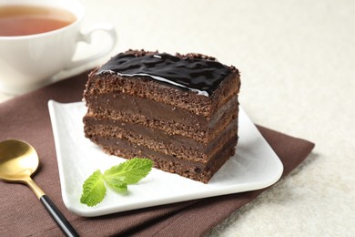 Photo of Piece of chocolate cake served with mint, spoon and tea on white table, closeup