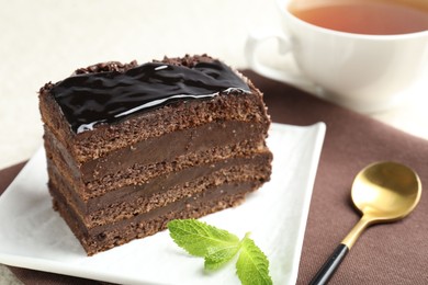 Photo of Piece of chocolate cake served with mint and spoon on table, closeup
