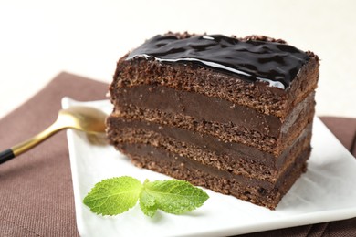 Photo of Piece of chocolate cake served with mint and spoon on table, closeup