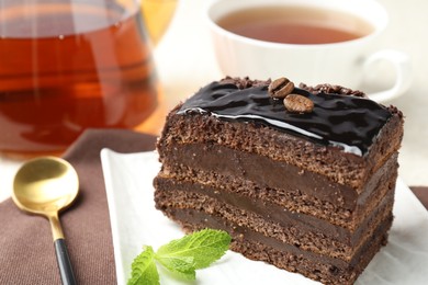 Photo of Piece of chocolate cake served with mint, spoon and tea on table, closeup