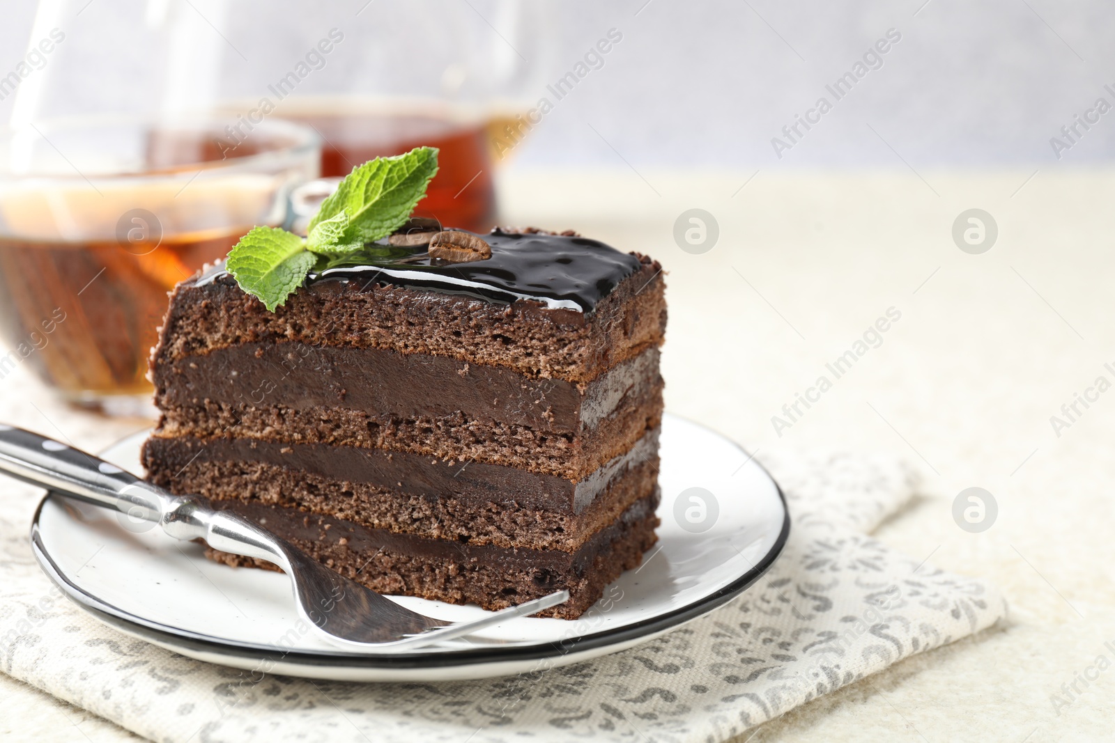 Photo of Piece of chocolate cake served with mint, fork and tea on white table, closeup. Space for text
