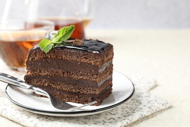 Photo of Piece of chocolate cake served with mint, fork and tea on white table, closeup. Space for text