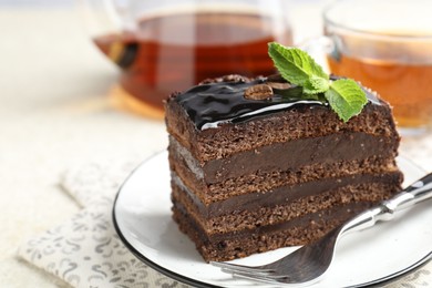 Photo of Piece of chocolate cake served with mint, fork and tea on white table, closeup. Space for text