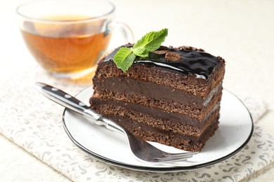 Photo of Piece of chocolate cake served with mint, fork and tea on white table, closeup