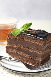 Photo of Piece of chocolate cake served with mint, fork and tea on table, closeup