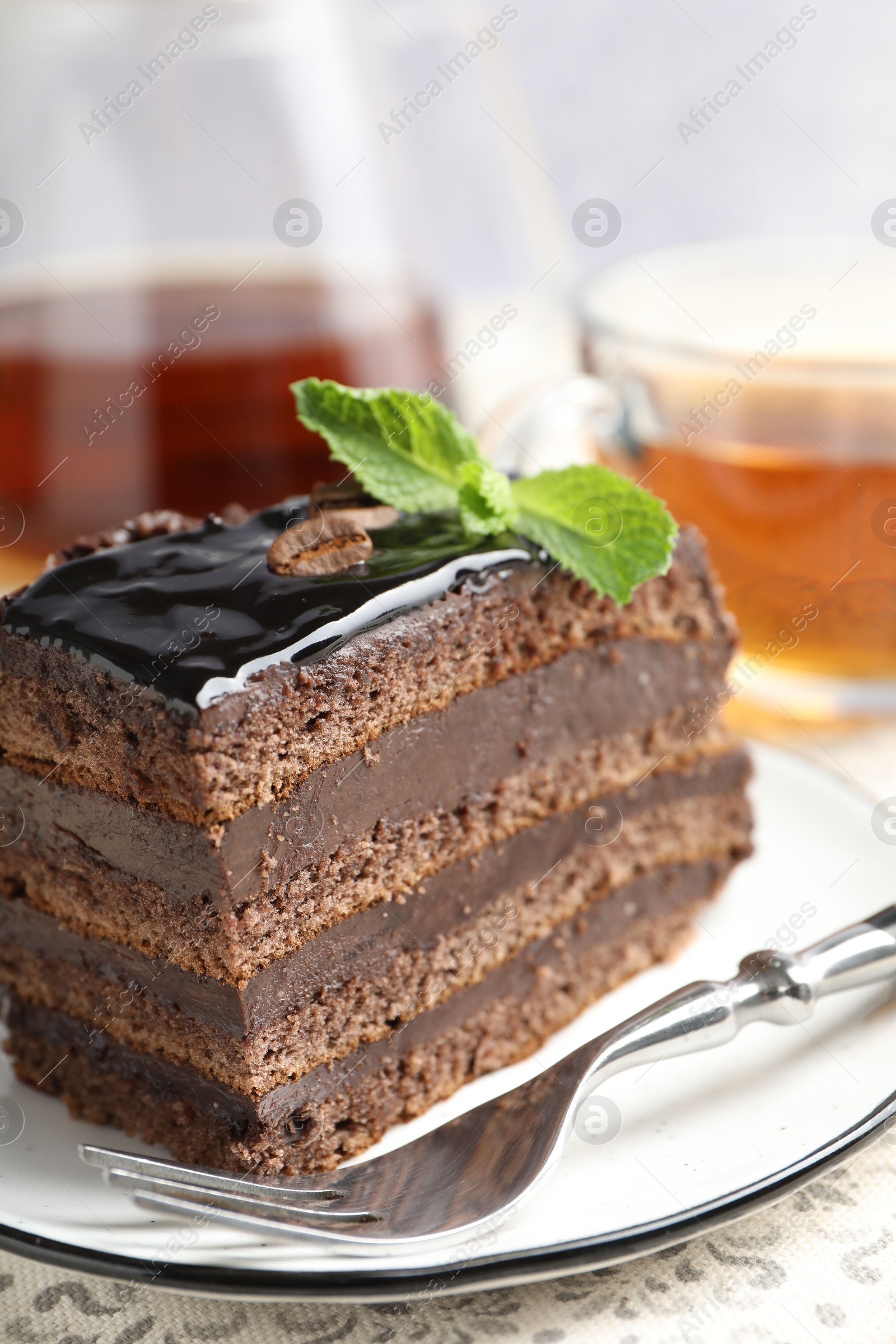 Piece of chocolate cake served with mint, fork and tea on table, closeup Photo of Piece of chocolate cake served with mint, fork and tea on table, closeup