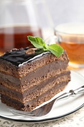 Photo of Piece of chocolate cake served with mint, fork and tea on table, closeup