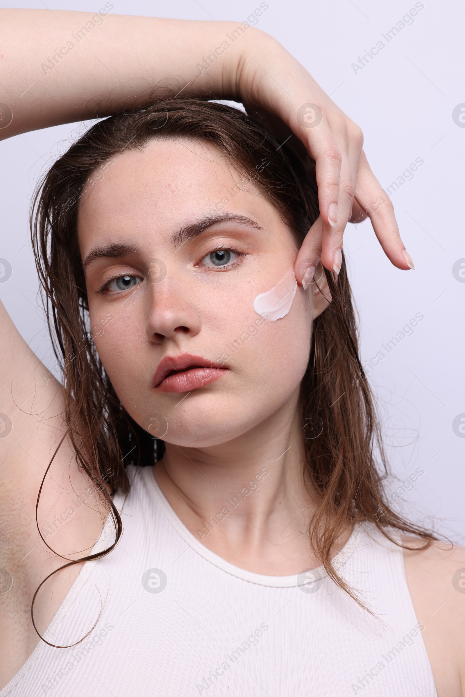 Beautiful woman applying skincare product onto her face on light grey background, closeup Photo of Beautiful woman applying skincare product onto her face on light grey background, closeup