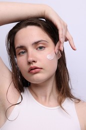 Photo of Beautiful woman applying skincare product onto her face on light grey background, closeup