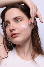 Photo of Beautiful woman applying skincare product onto her face on light grey background, closeup