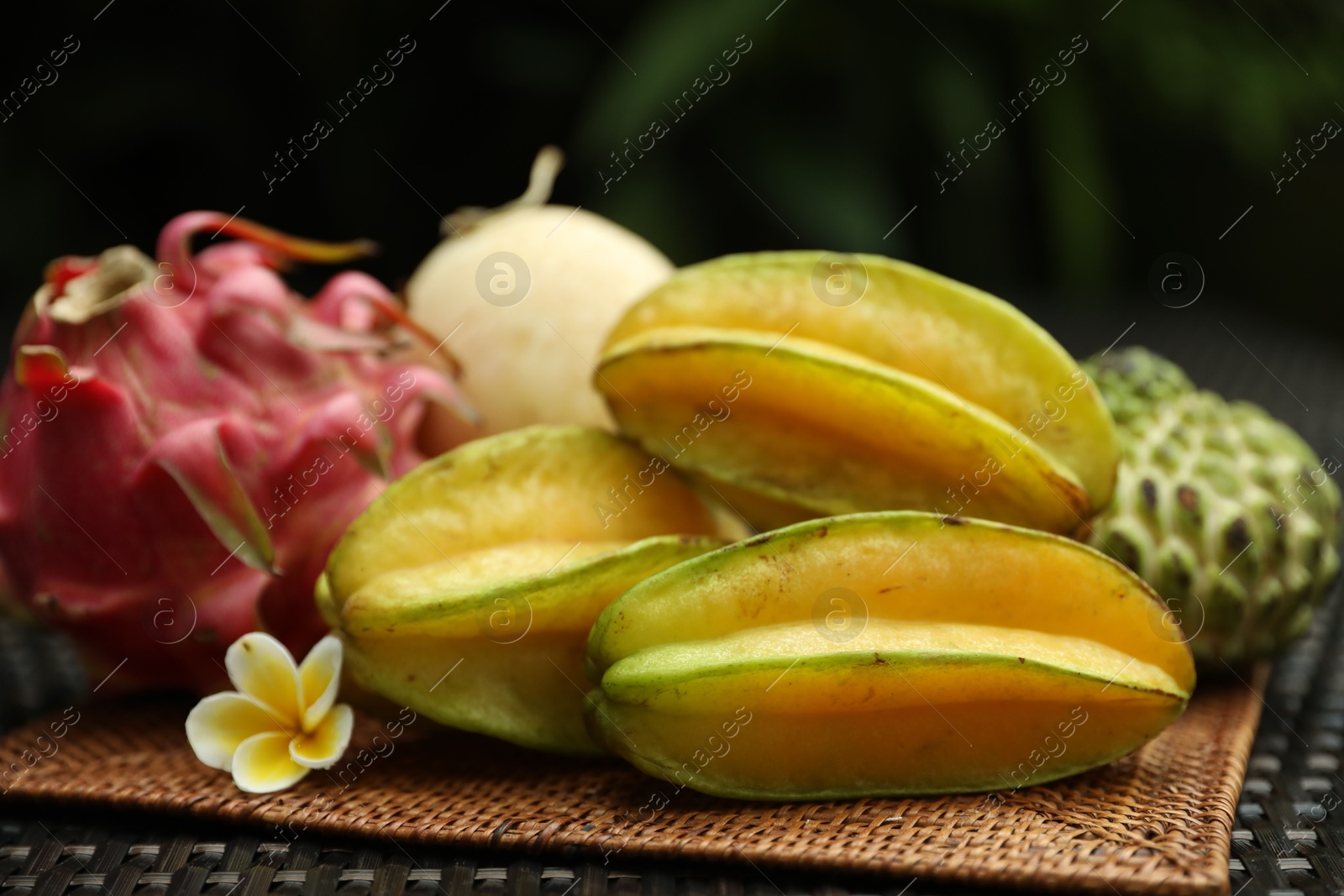Photo of Different tropical fruit on wicker table outdoors, closeup