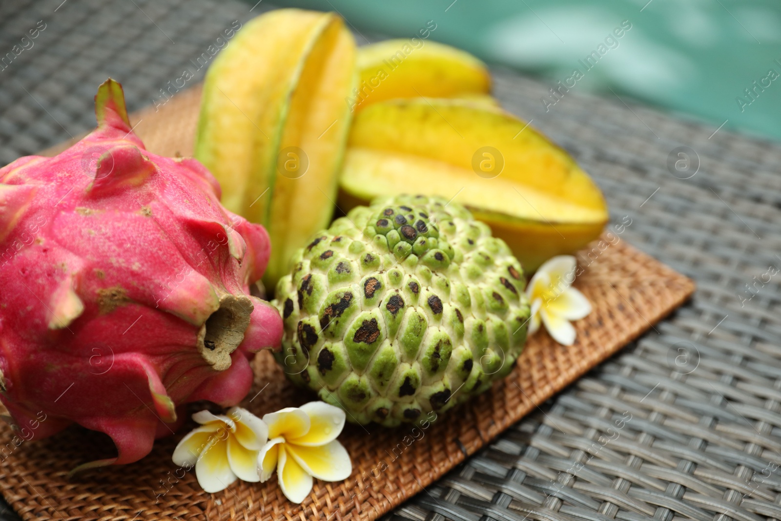 Different tropical fruit on wicker table near swimming pool, closeup Photo of Different tropical fruit on wicker table near swimming pool, closeup