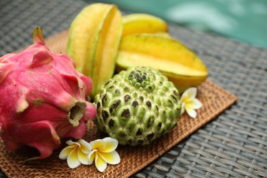 Photo of Different tropical fruit on wicker table near swimming pool, closeup