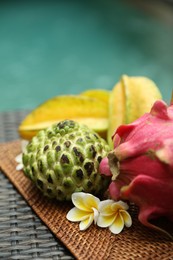 Photo of Different tropical fruit on wicker table near swimming pool, closeup. Space for text