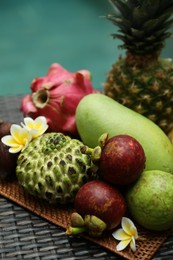 Photo of Different tropical fruit on wicker table near swimming pool, closeup
