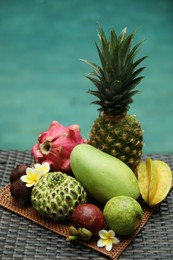 Photo of Different tropical fruit on wicker table near swimming pool