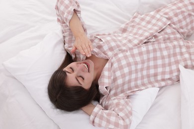 Photo of Sleepy woman yawning on bed at home, above view